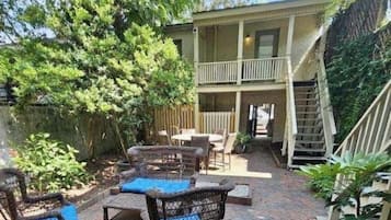 A two-story building with a balcony, outdoor seating area with wicker furniture, and a staircase leading to the upper level.