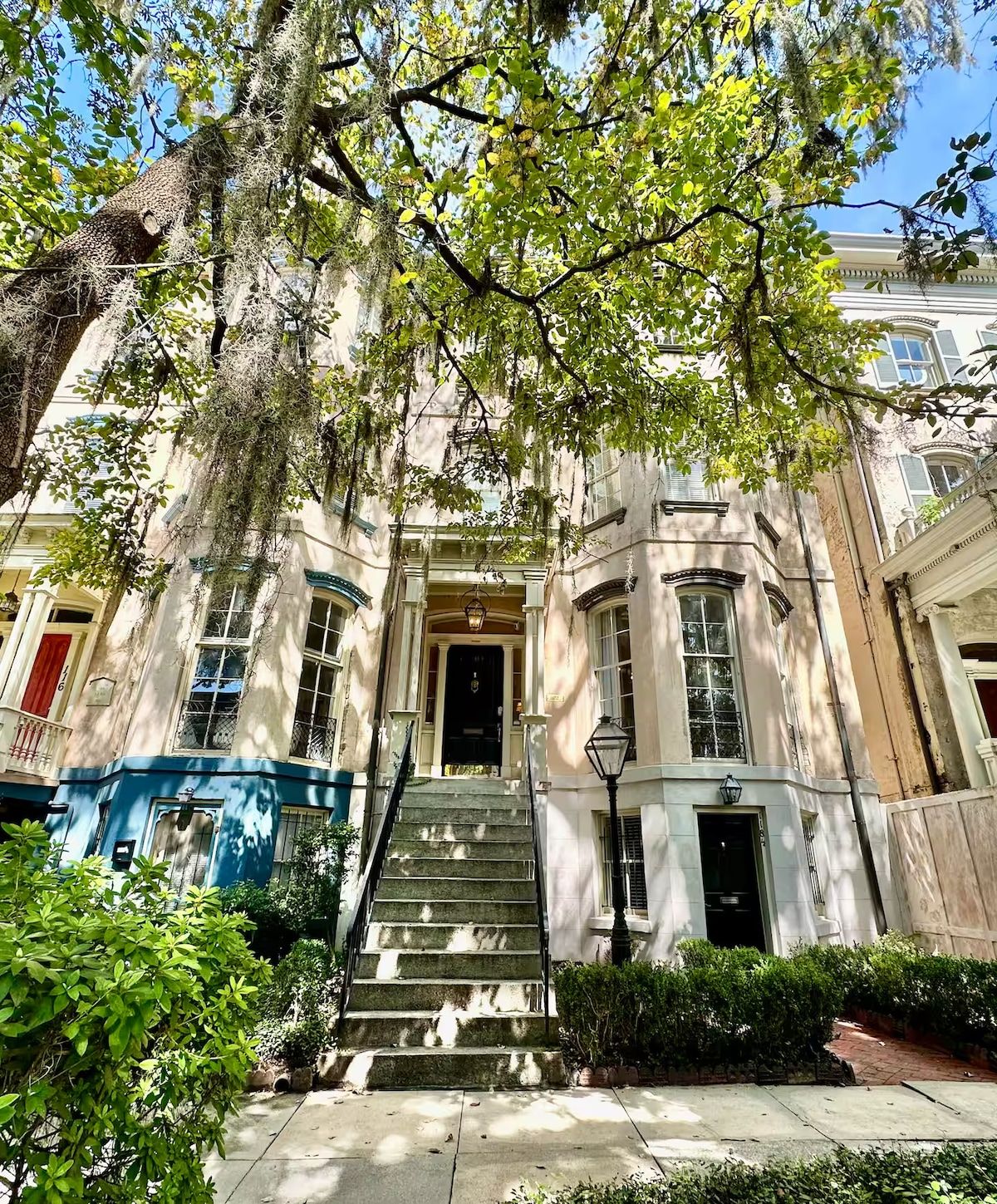 A historic building with a central entrance, a staircase leading up to it, and a surrounding garden.