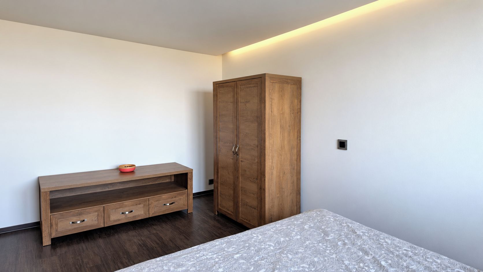 Une pièce comprenant une armoire en bois, un banc en bois doté de tiroirs et une couvre-lit à motifs.