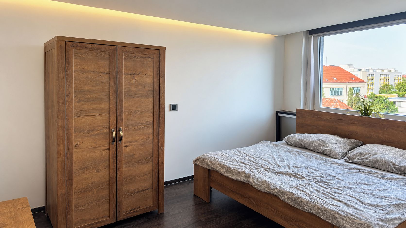 Un dormitorio con un armario grande, una cama con ropa de cama estampada y una ventana con vistas a edificios.