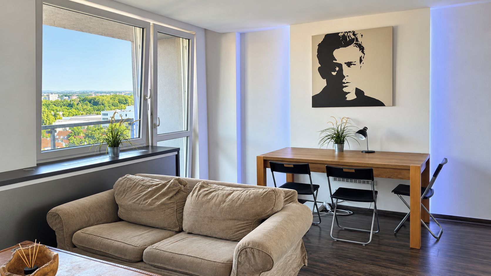 Un salon moderne avec un canapé, une table à manger et des chaises, une plante en pot et une vue sur la ville par la fenêtre.