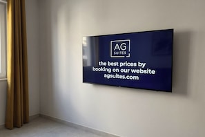 A flat-screen TV mounted on a wall displaying a promotional message for AG Suites. - Rocha Golden Cliff by Agsuites com (Praia da Rocha)