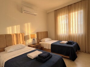Una habitación de hotel con dos camas, una mesita de noche, una lámpara y un equipo de aire acondicionado.