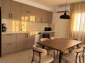 A modern kitchen with a dining area, featuring a wooden table and chairs, a coffee maker, and an air conditioning unit. - Rocha Golden Cliff by Agsuites com (Praia da Rocha)