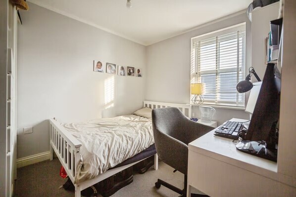 A bedroom with a single bed, a desk with a computer, a chair, and a window with blinds. - Apartment Sleeps 4 with Balcony (Erith)
