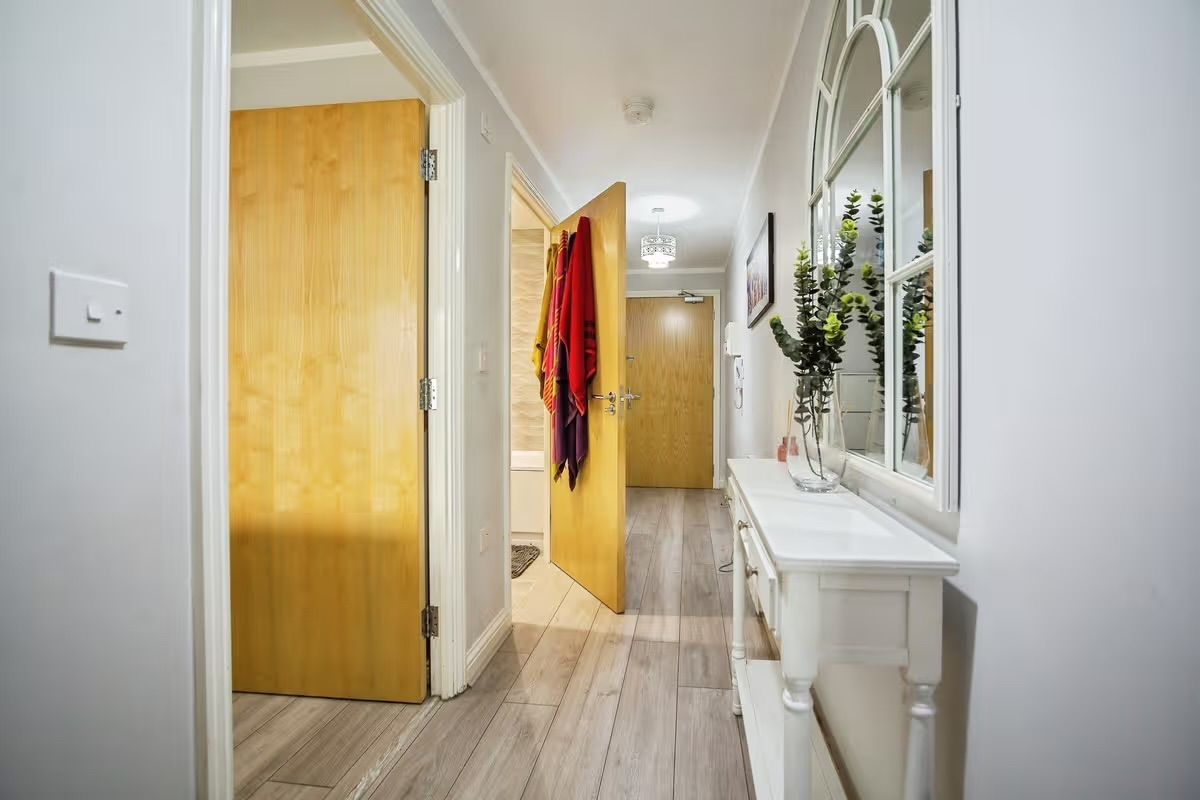 A hallway with wooden doors, a white vanity with a mirror, and a plant.