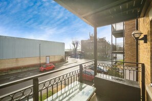 A balcony with a view of a street, a building with a metal fence, and a brick wall. - Apartment Sleeps 4 with Balcony (Erith)
