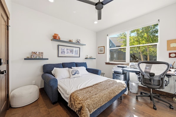 Un dormitorio con cama, escritorio, silla y ventana.
