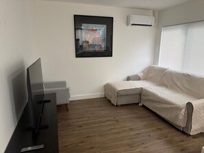 A living room with a flat-screen TV, a beige sofa, a framed artwork on the wall, and an air conditioning unit. - Newly Renovated 1BR | Near Beach & Downtown #3 (Hollywood)