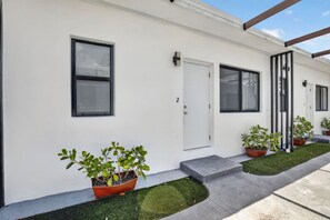 Un edificio moderno con paredes exteriores blancas, puertas numeradas y plantas en macetas a lo largo de la fachada.