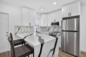 A modern kitchen with white cabinetry, a marble countertop island, a stainless steel refrigerator, and a microwave. - Newly Renovated 1BR | Near Beach & Downtown Unit 2 (Hollywood)