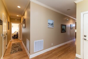 A hallway with wooden flooring, beige walls, and several framed pictures. - Cheehaw Paradise | 2 Min Beach Walk | Elevator | Dual King Suites | Sleeps 14 | Dog Friendly (Edisto Beach)