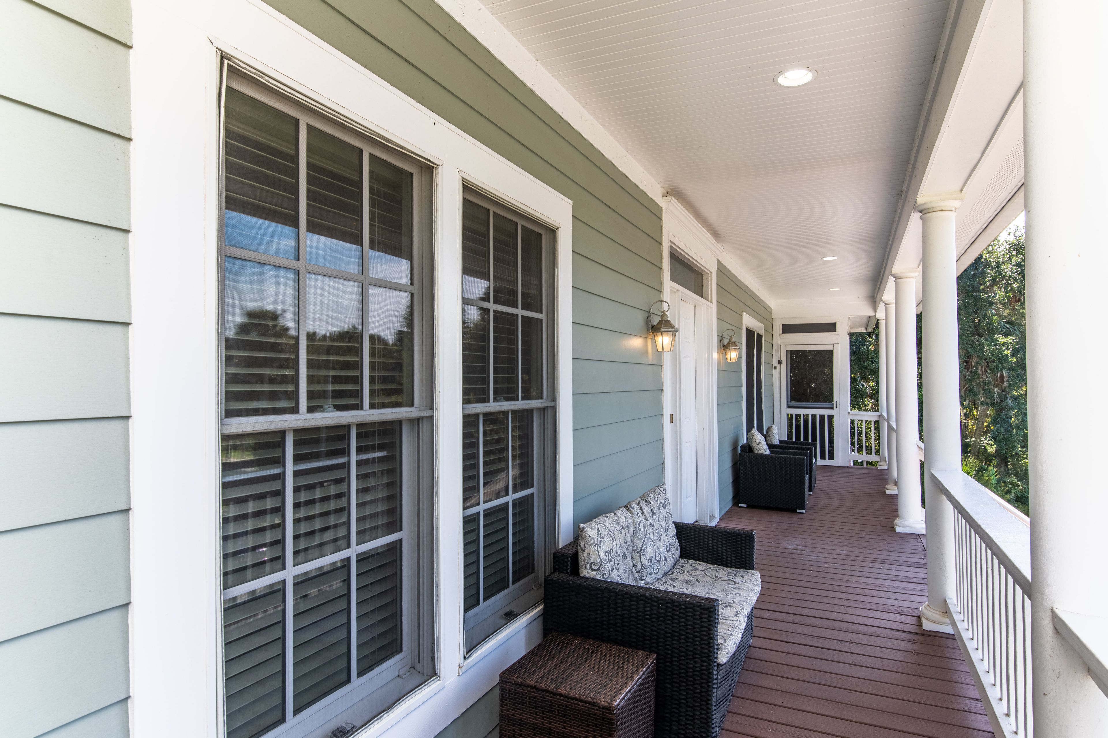 A covered porch with a row of windows, wicker furniture, and a wooden deck.