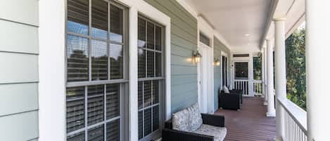 A covered porch with a row of windows, wicker furniture, and a wooden deck.