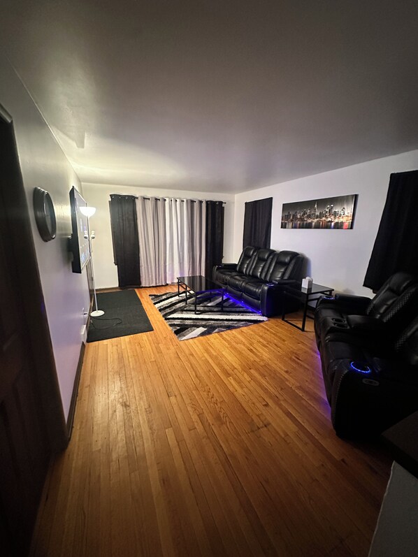 Una sala de estar con un sofá de cuero negro, una mesa de centro y un cuadro de un paisaje urbano en la pared.