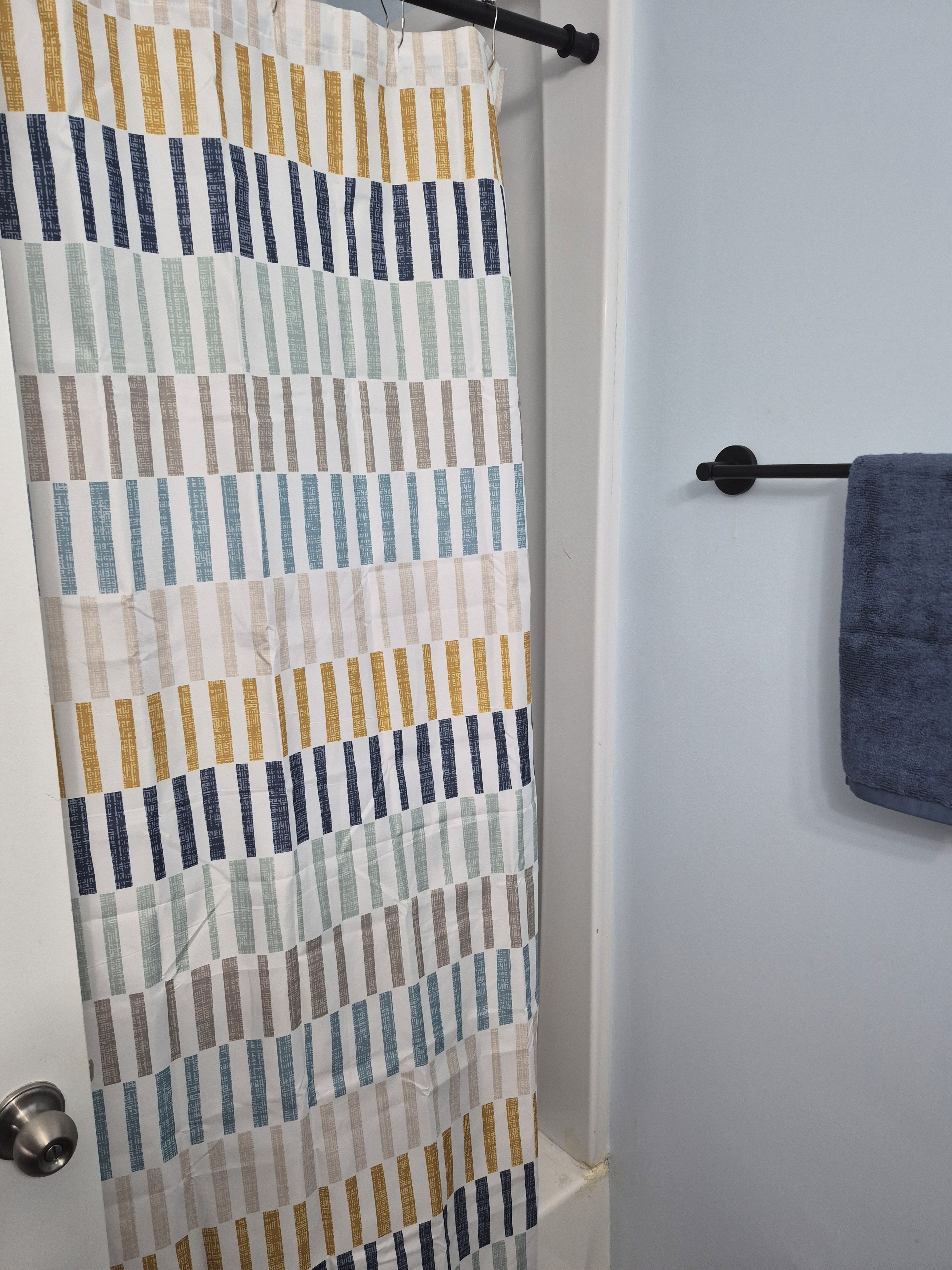 Un baño con cortina de ducha a rayas, un perchero con una toalla y una puerta con pomo metálico.