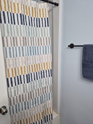 Een badkamer met een gestreepte douchegordijn, een handdoekrek met een handdoek en een deur met een metalen handgreep.