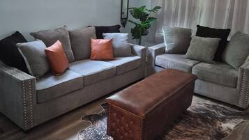 A living room with a grey sofa, a brown ottoman, and a ceiling fan.