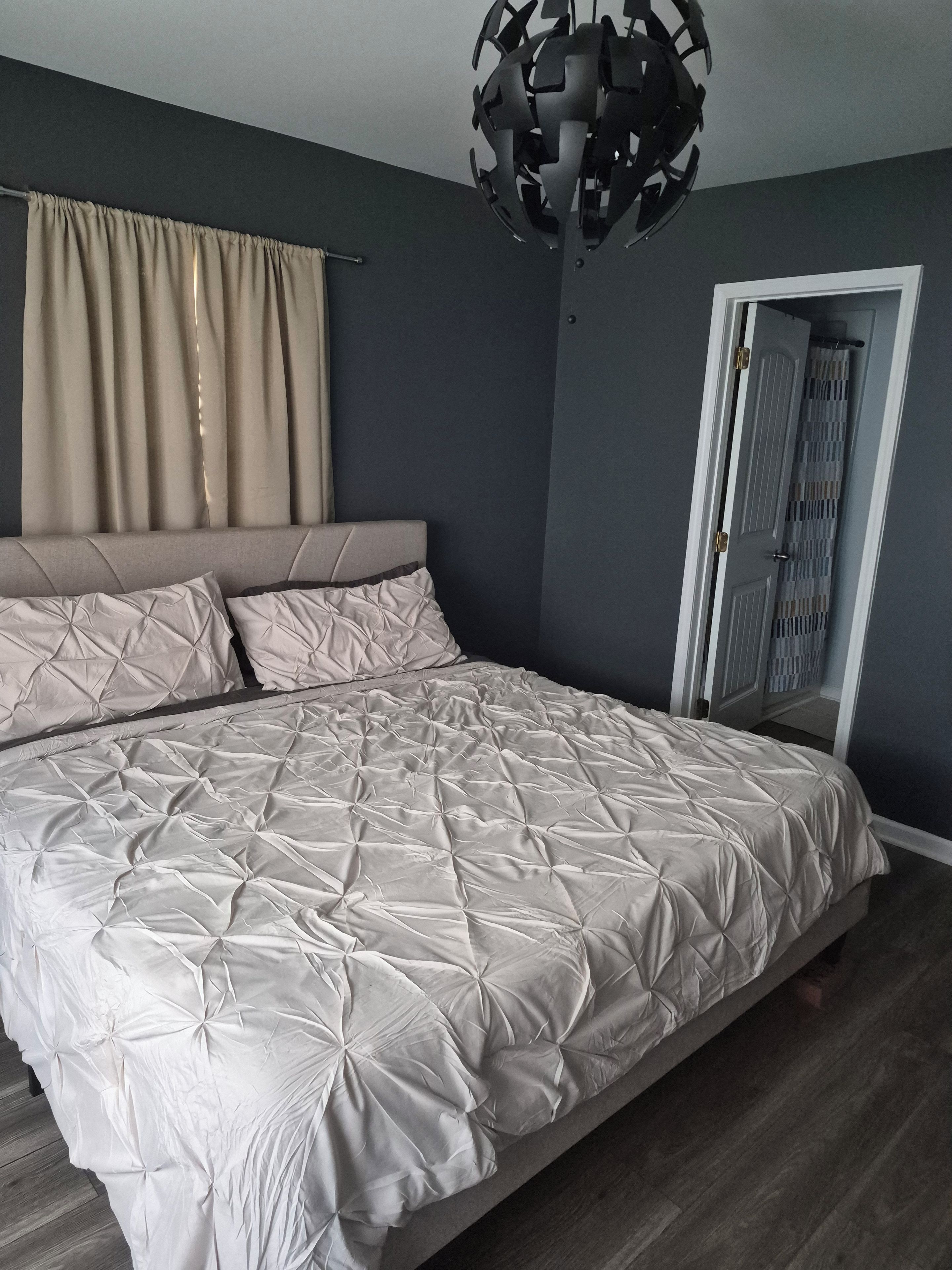 Un dormitorio con cama, cortinas, un espejo y una puerta.