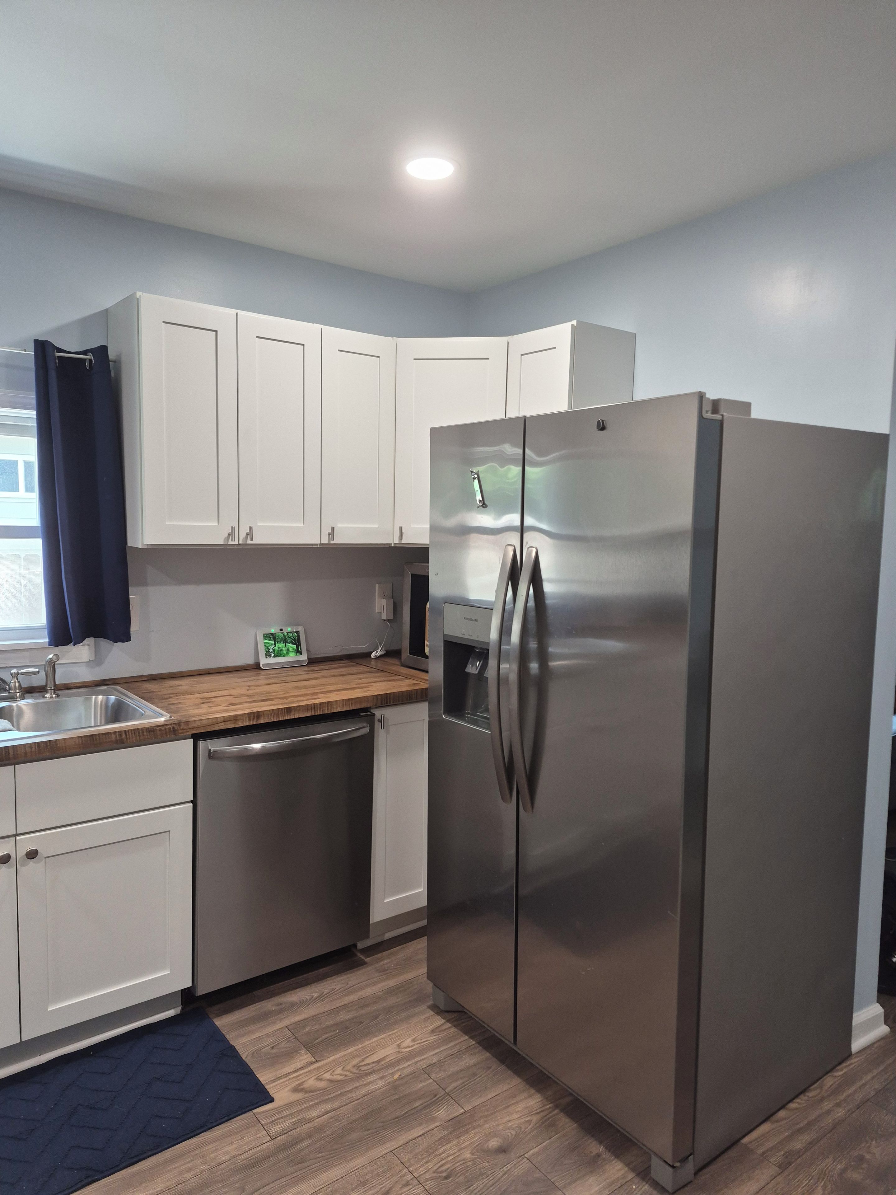 A modern kitchen with stainless steel appliances, white cabinetry, and a wooden countertop.