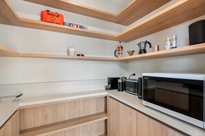 Una cocina moderna con armarios de madera, un microondas, una cafetera y una estantería con utensilios básicos de cocina.