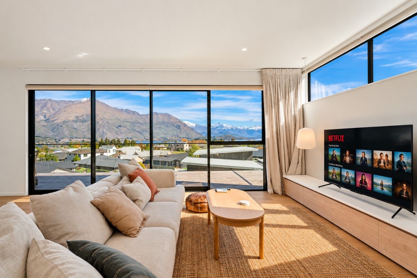 A modern living room with a large TV, a sofa, a coffee table, and a view of mountains through large windows.