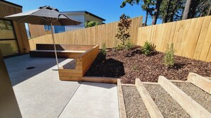 A wooden deck with a built-in bench, a small garden area with mulch and plants, and a wooden fence. - Elevated Lake Wānaka Retreat | 4 Bedrooms, 3 Bathrooms, Fireplace & Panoramic Views (Wānaka)