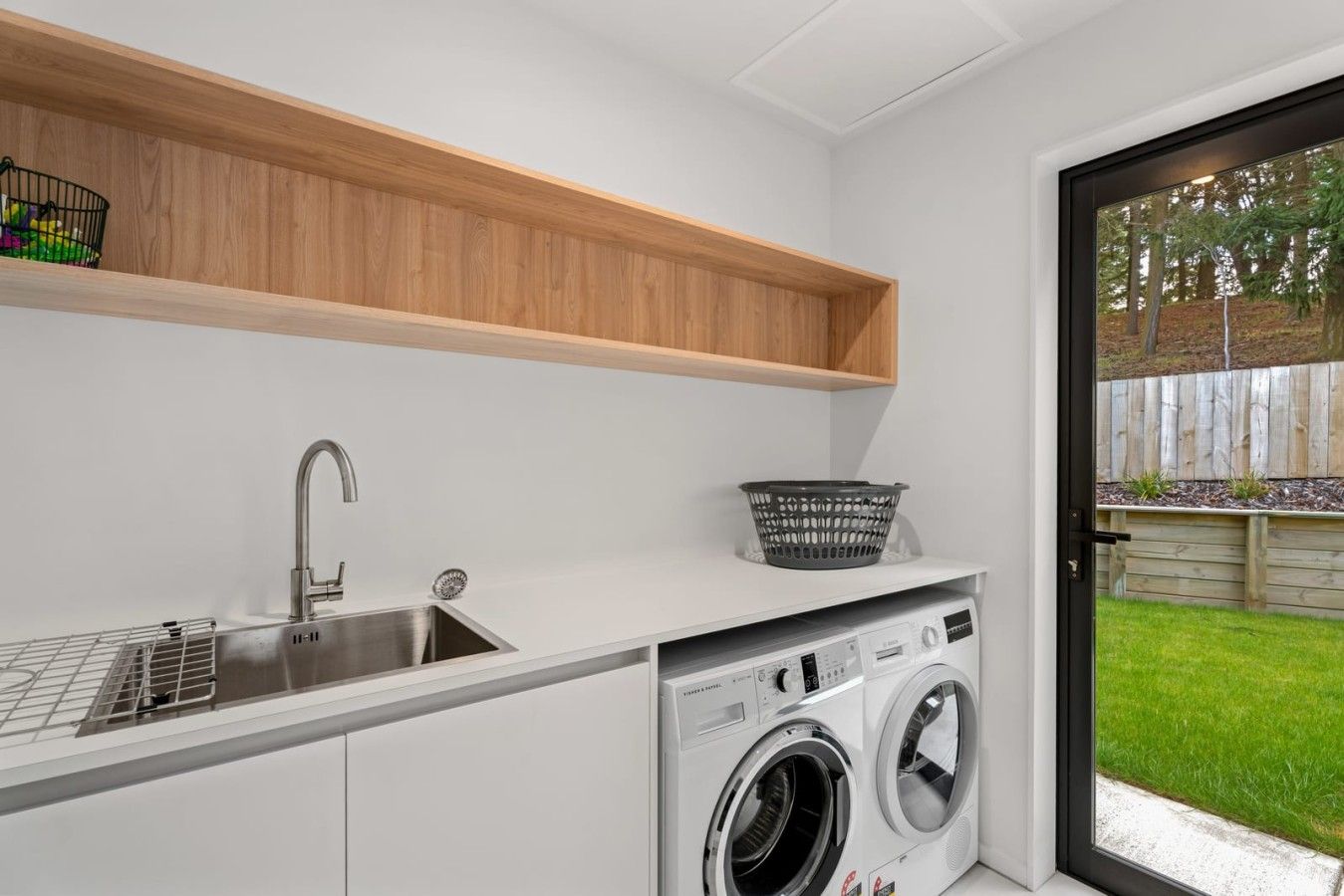 A laundry area with a washing machine, a sink, and a shelf with a basket.