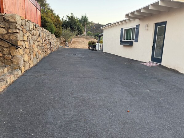 A paved driveway leading to a building with a stone wall on one side and a white exterior with dark shutters.