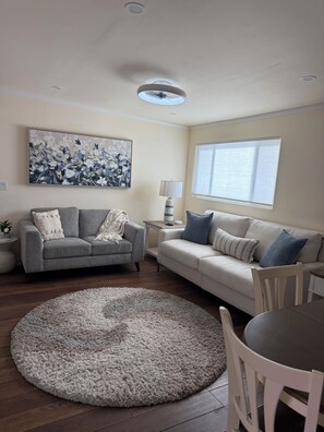 Ein Wohnzimmer mit grauem Sofa, weißem Sofa, rundem Teppich und Tisch mit Stühlen.