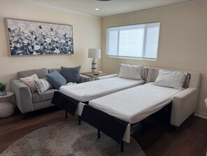 A hotel room with two beds, a sofa, a lamp, a painting, and a window.