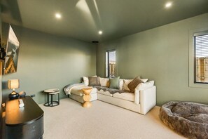Ein Wohnzimmer mit einer Eckcouch, einem runden Couchtisch, einem Haustierbett und einer Wandlampe.