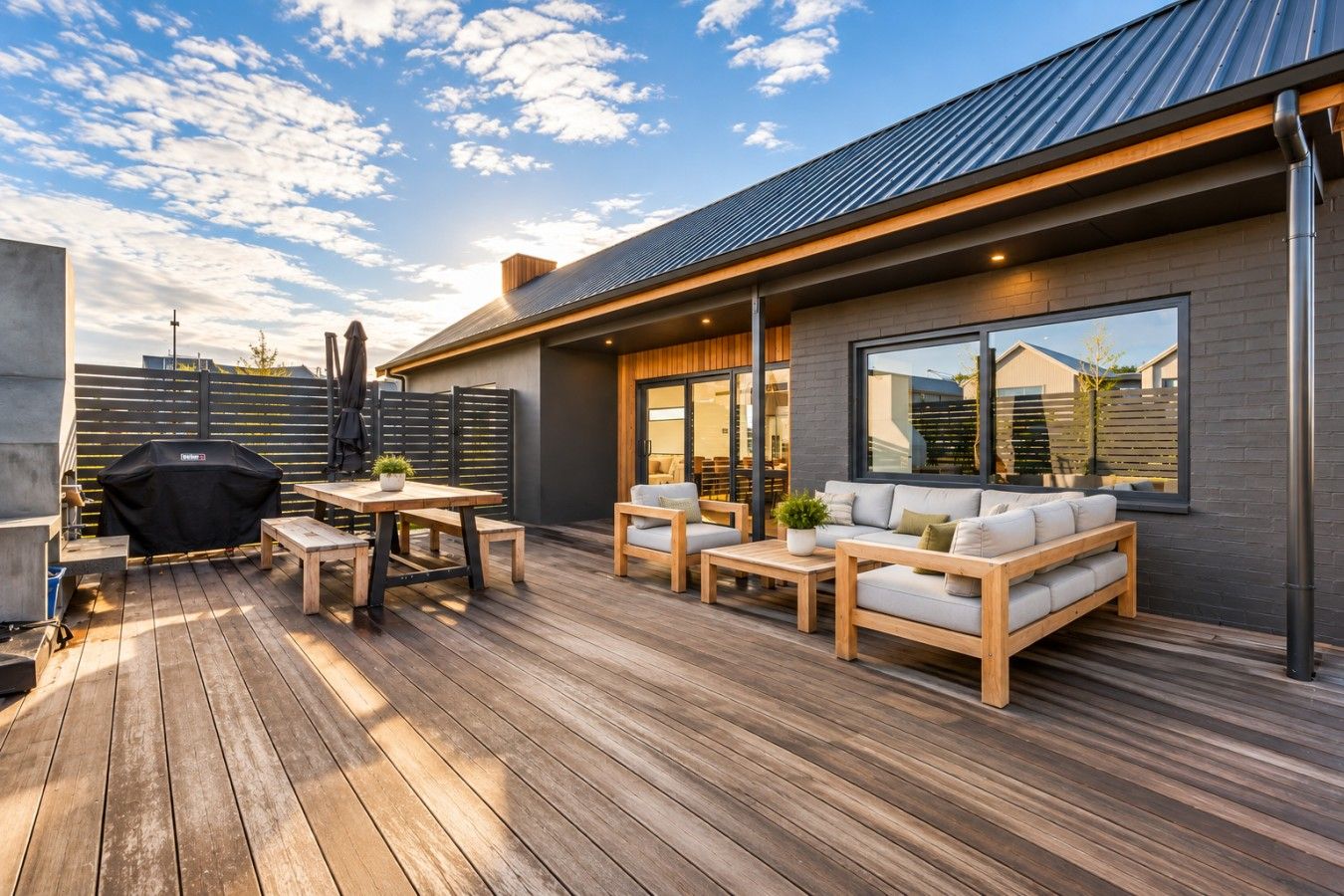 A modern outdoor patio with a wooden deck, a barbecue grill, and outdoor seating.