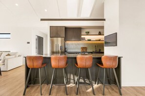 Eine moderne Küche mit einer zentralen Kochinsel, Barhocker und einem Essbereich mit einer Couch.