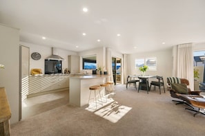 A modern kitchen with a central island, a dining area with a table and chairs, and a living space with a sofa and armchair. - Mountain View House | 3 Bedrooms, Sleeps 6, 2 Bathrooms, Air Conditioning & Easy Access to Lake Wānaka (Wānaka)
