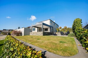 A modern two-story house with a stone foundation, a covered patio, and a well-maintained lawn. - Mountain View House | 3 Bedrooms, Sleeps 6, 2 Bathrooms, Air Conditioning & Easy Access to Lake Wānaka (Wānaka)