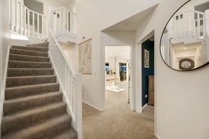 A carpeted staircase with white railings leading to a second floor. A hallway with a mirror and a door labeled 'CICO BELLA' is visible. - Mountain View House | 3 Bedrooms, Sleeps 6, 2 Bathrooms, Air Conditioning & Easy Access to Lake Wānaka (Wānaka)