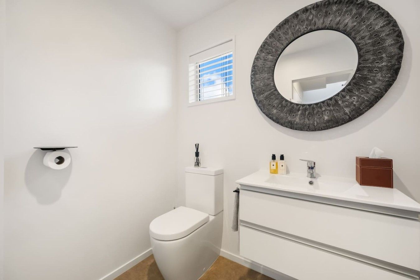 Een badkamer met een toilet, een wastafel met spiegel en een raam met zonwering.