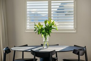 A round dining table with a vase of flowers in the center, surrounded by chairs. - Mountain View House | 3 Bedrooms, Sleeps 6, 2 Bathrooms, Air Conditioning & Easy Access to Lake Wānaka (Wānaka)