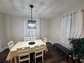 A dining area with a table, chairs, a bench, a hanging light fixture, and a potted plant.