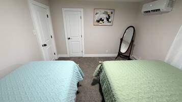 A bedroom with two beds, a door, a mirror, and an air conditioning unit.