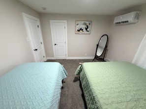 Une chambre avec deux lits, une porte, un miroir et un appareil de climatisation.