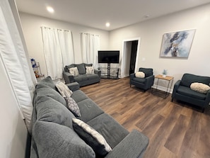A modern living room with a grey sectional sofa, a small grey armchair, a coffee table, and a flat-screen TV.