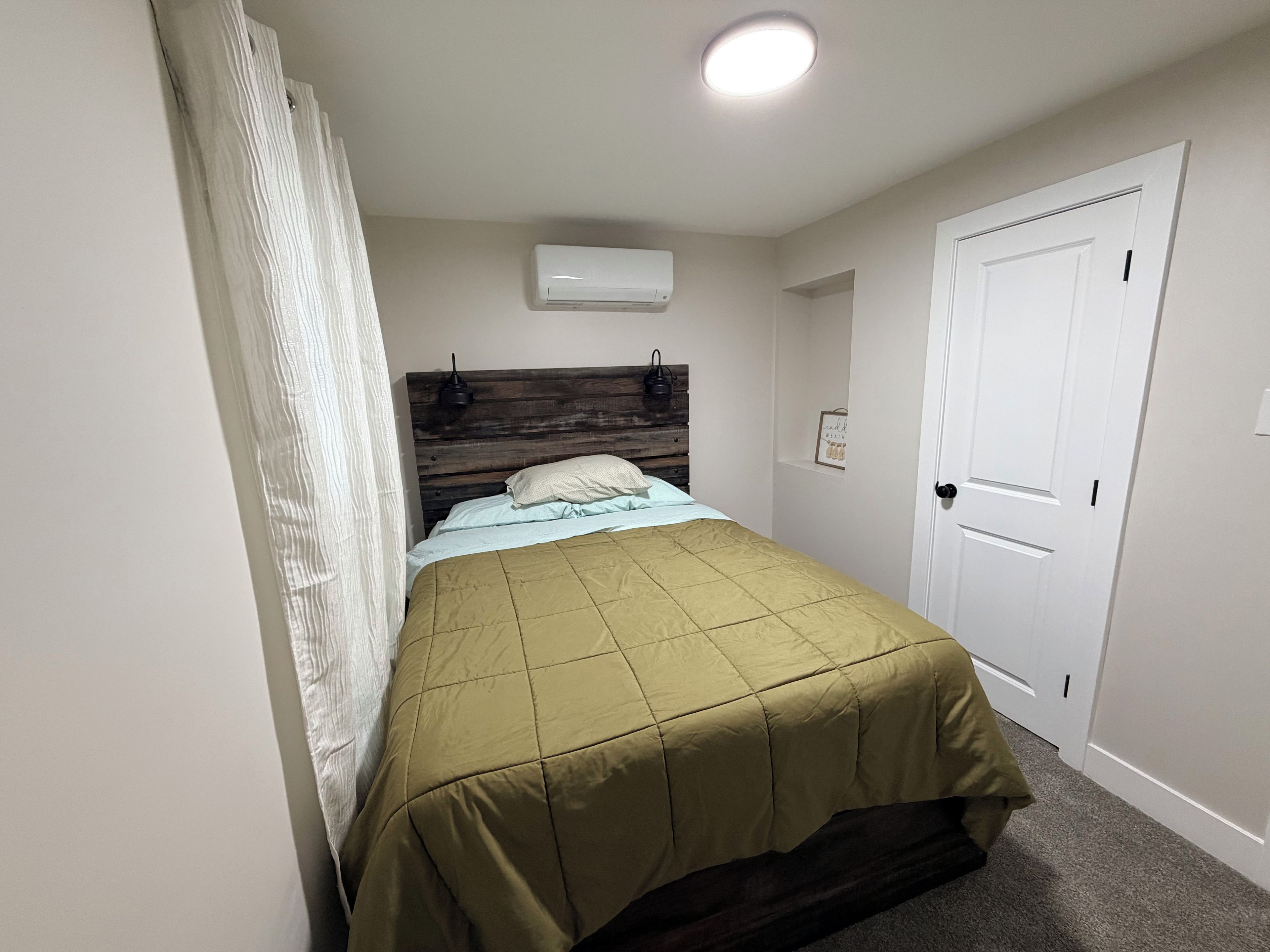 Ein Schlafzimmer mit einem Bett, einem Holzkopfende, einer Klimaanlage, einer Tür und einer Leuchte.