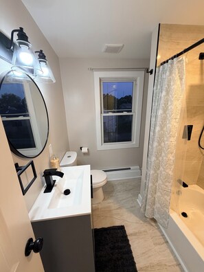 A modern bathroom with a toilet, sink, and bathtub. There is a window with a view of the outside, and a shower curtain.