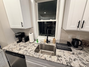 A kitchen with a stainless steel sink, a toaster, a paper towel holder, and a window with a view of a person in the background.