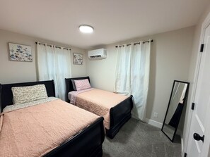 A bedroom with two beds, a ceiling light, an air conditioning unit, and a mirror.