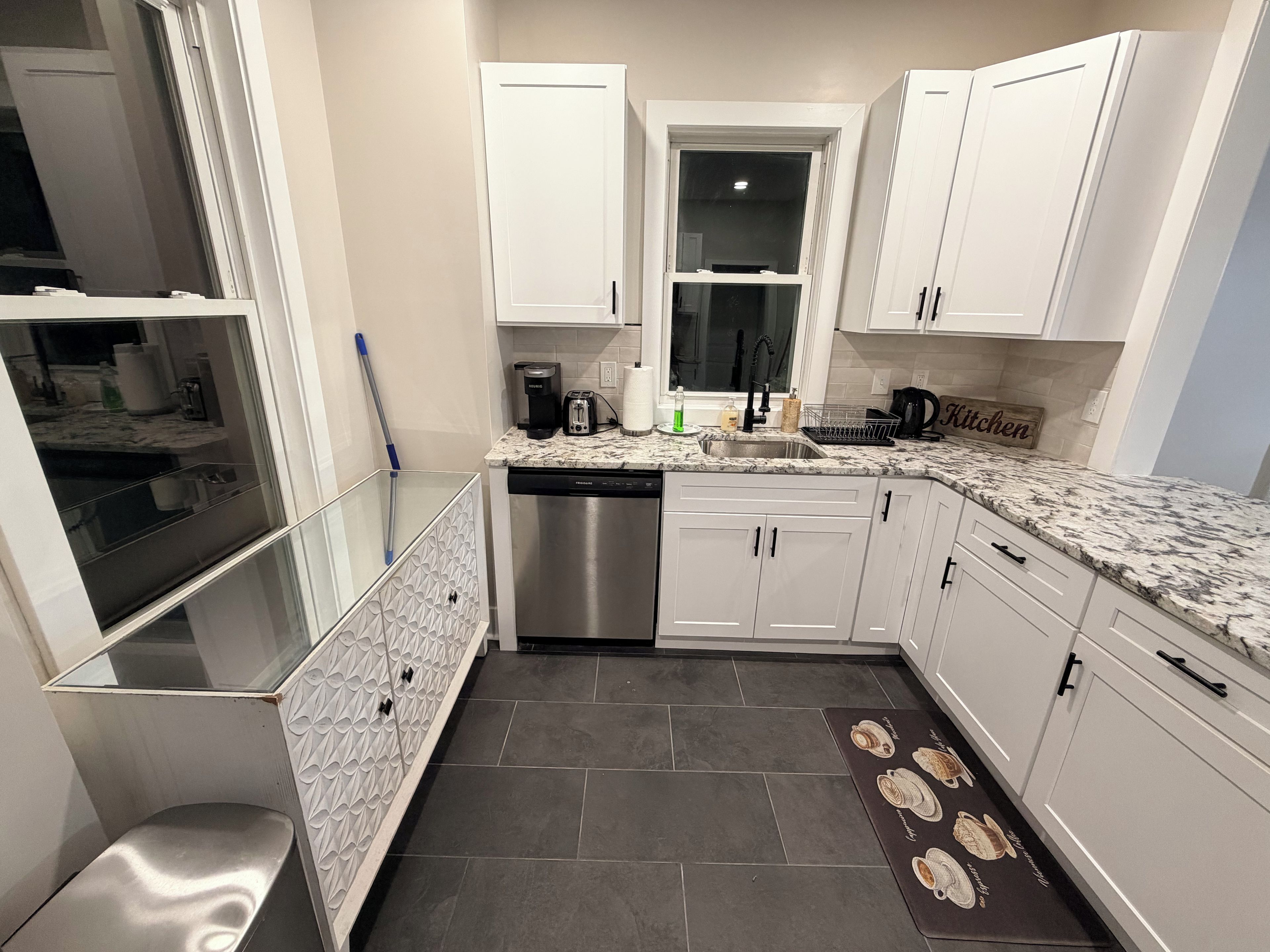A modern kitchen with white cabinets, a stainless steel dishwasher, and a marble countertop.