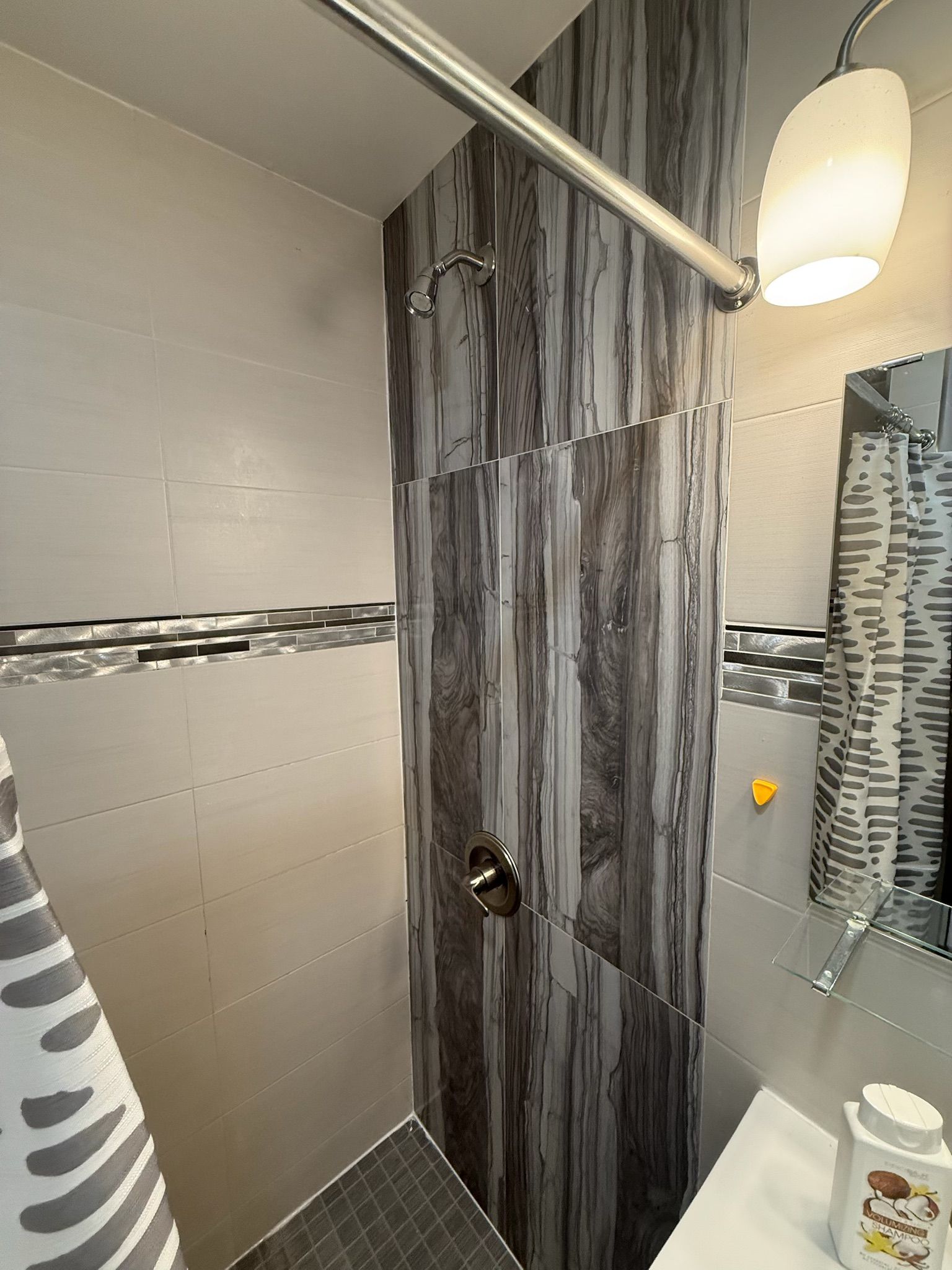 Een douche met een glazen deur, een handdoekhouder, een spiegel en een douchegordijn.