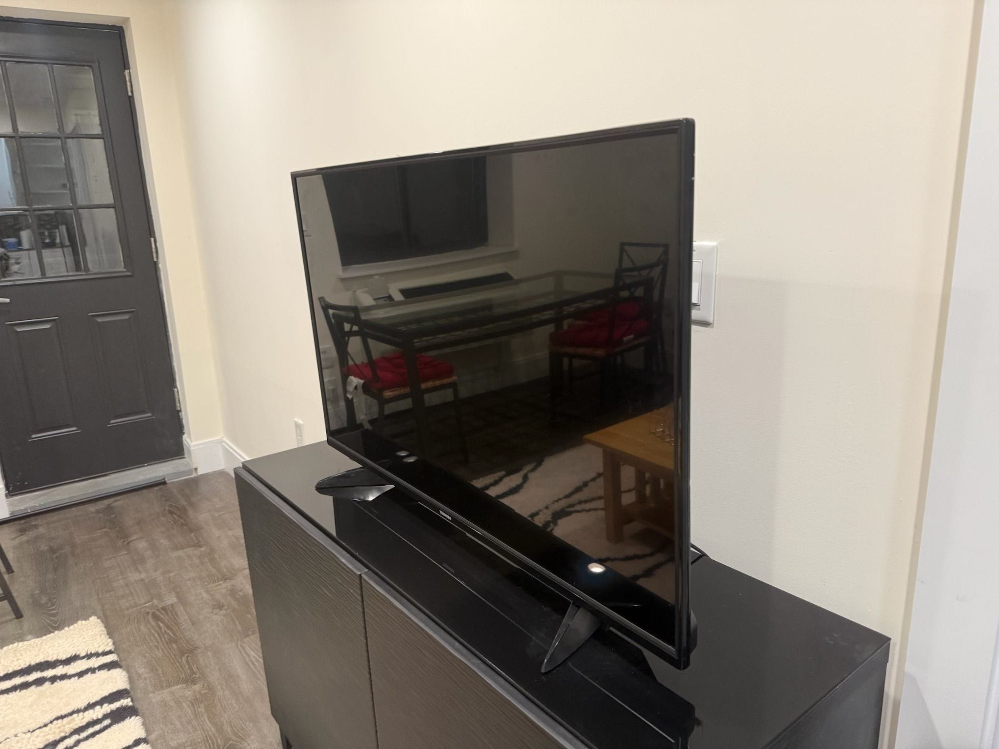 A flat-screen TV mounted on a black entertainment center in a room with a dining area visible through the glass door.